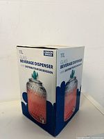 Front and side views of the boxed beverage dispenser showing product branding and packaging details.