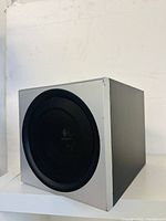 Front and angled views of the Logitech Z-2300 subwoofer showing its silver front panel, black protective grille, and Logitech logo.