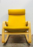 Front view of the yellow upholstered rocking chair with birch veneer frame showing seat, backrest, armrests, and headrest cushion.