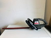 Side view of small black and gray Craftsman 20 electric hedge trimmer with blade resting on white surface, rust visible on blade.