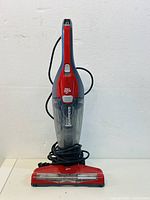 Front view of the red and black Dirt Devil handheld vacuum cleaner with clear dust container, cord wrapped around the base.