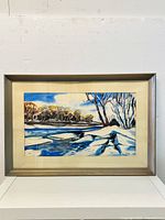 Front view of framed winter landscape watercolor wall art, mounted in a silver-tone frame with beige matting.