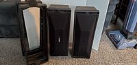 Front and side view of two Bose 402 professional loudspeakers and one carry case, all black.