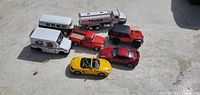Seven large friction cars and vehicles on concrete ground including vans, trucks, and sports cars.