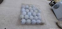 Clear plastic bag containing approximately 36 used white golf balls laid on a light-colored surface with some background items visible.