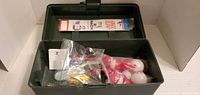 Open black plastic tackle box showing red and white bobbers, fishing hooks in plastic bags, and a fishing line pack inside.