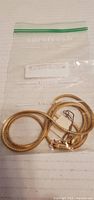 Gold tone snake chain necklace coiled inside a clear plastic bag with a label seen behind it.