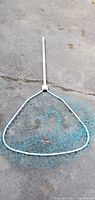 Large white metal framed fishing net with blue nylon mesh lying flat on asphalt ground.