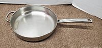 Top view of large stainless steel Farberware frying pan with visible wear marks inside and handles attached.