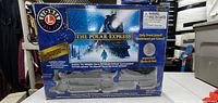 Front of the boxed Lionel The Polar Express Train Cars set showing branding, product name, and some product features such as including Santa’s bell and being battery powered.
