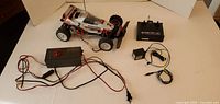 R/C toy car with wired charger, remote controller, and batteries shown on white surface.