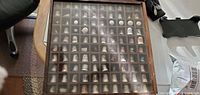 Wooden display case containing approximately 60 assorted decorative thimbles each in individual compartments covered by glass.