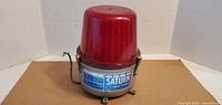 Front view of vintage Saturn Safety Light Reflecto emergency beacon light showing label on metal base, attached wiring, and red dome lens.