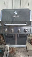 Front view of the Dyna-Glo BBQ with main lid closed, three knobs and ignitor control on front panel, built-in temperature gauge on lid center, and storage doors below.