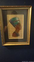 Framed Egyptian painting showing a profile portrait on papyrus mounted on blue mat within a gold frame.