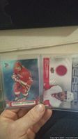 Photo showing two hockey cards in sleeves, one card features Henrik Zetterberg in red uniform skating, the other a memorabilia card with a red fabric swatch.