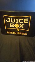 Closed box showing Juice Box Rosin Press branding in black and yellow.