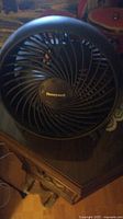 Photo of a small black Honeywell table fan placed on wooden furniture showing the front grille and blade design.