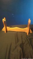 Wooden sword stand with two upright supports and a curved base, photographed front on against a dark background.
