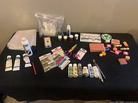 Full lot showing paints, stamps, bath bomb moulds, scissors, brushes, glues, and plastic sheets laid out on a black tablecloth.