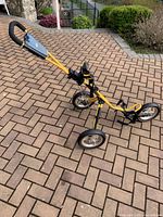 Yellow Bag Boy Express golf push cart standing on paved driveway, showing ergonomic handle and air ride system.