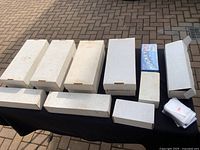 Eight white cardboard boxes and two sleeve boxes arranged on black table outdoors