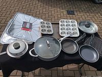 Overview of cookware set arranged on table showing pots, pans, muffin tins, and disposable baking trays.