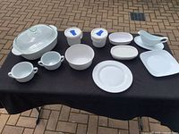Full set of Corningware Plus white ceramic bakeware and tableware items laid out on black cloth, visible in good condition