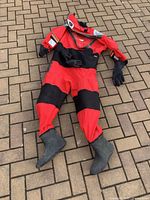 Full body shot of red and black dry suit laid out showing attached gloves and boots on paved surface