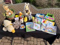 Full overview of the lot laid out on a black cloth outside on a patio showing plush toys, baskets, children's books, and craft items arranged for display.
