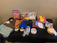 Wide shot of fabric pieces, ribbons, stuffing, pom-poms, and craft book on black surface.