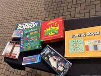 Overview of six games placed on table including Sorry, Apples to Apples, Soccer Tactics World, Rummy Royal, Master Mind, and Cribbage score pad.