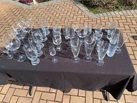 Top view of a table covered with black cloth displaying an assortment of clear glassware including wine glasses, champagne flutes, and bowls arranged in groups.