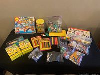 Full lot view showing the variety of crafting supplies on a black table including bead containers, Shrinky Dinks packages, markers, clay sticks, glitter, and airplane kit.