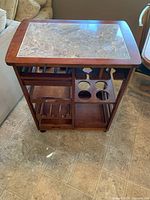 Front view of wooden kitchen island with marble top showing wine and bottle storage cutouts and tray shelf.