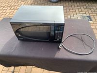 Full view of the black microwave oven with windowed door, digital control panel, and power cord.