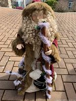 Full view of the Santa figurine standing outdoors on a paved surface, showing outfit, staff, and accessories.