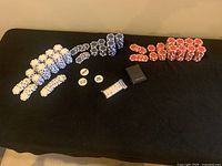 Poker set contents laid out on black surface, showing white, red, and blue poker chips, dealer and blind chips, and playing cards in plastic wrap.