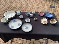 Overview of all pottery and china items on black cloth: 13 pieces including various bowls, plates, jugs, vases, and Royal Albert tea cup set