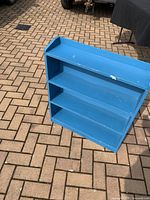 Front view of small blue wooden bookshelf showing three shelves and some paint damage