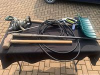 All items laid out on black cloth on table: sledgehammer, electric drill, pressure washer wand with hose, snow shovel, metal bar