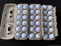 Top-down view of three egg cartons filled with white golf balls, showing wear and varied brands.