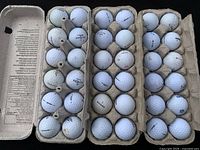 Top view of three open cartons filled with assorted used golf balls showing brand names and wear.