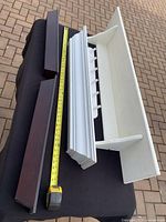 Three wall shelving units laid out on black cloth with tape measure to show sizes.