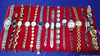 15 assorted women's wristwatches laid out side-by-side on red fabric background showing variety of bands and watch faces