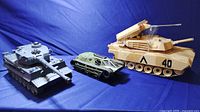 Three vintage toy tanks: large grey Tiger tank, green RipSaw 1/24 scale, tan remote control tank with missile launchers.