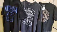 Three rock band T-shirts hanging side by side: Nirvana, Guns N' Roses, AC/DC
