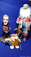 Three figurine statues on blue background: George Bush electronic bobblehead, Ziggy golfer figurine, and Santa fisherman figurine.