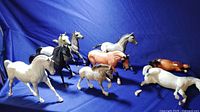 Nine Breyer horse figurines arranged on a blue background, showing variety in colors and poses including white, black, grey, and spotted appaloosa.