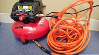 Front view of Central Pneumatic 3 gallon 100 PSI oil-less air compressor with orange coiled hose attached.